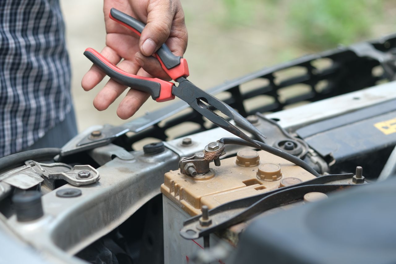 Crafting Captivating Headlines: Your awesome post title goes here Person using pliers to check a car battery in an outdoor setting.